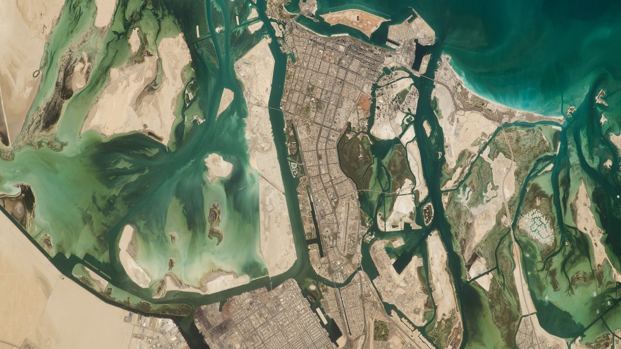 Stand-in, not a photo of this event: Abu Dhabi seen from the International Space Station in June 2023, with turquoise lagoons, green mangrove channels and pale desert flats wrapping around the grid of the island city along the Persian Gulf