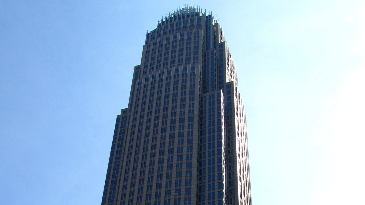 Stand-in, not a photo of this event: the upper floors and crown of the Bank of America Corporate Center tower in Charlotte, North Carolina, against a pale blue sky (June 2011)