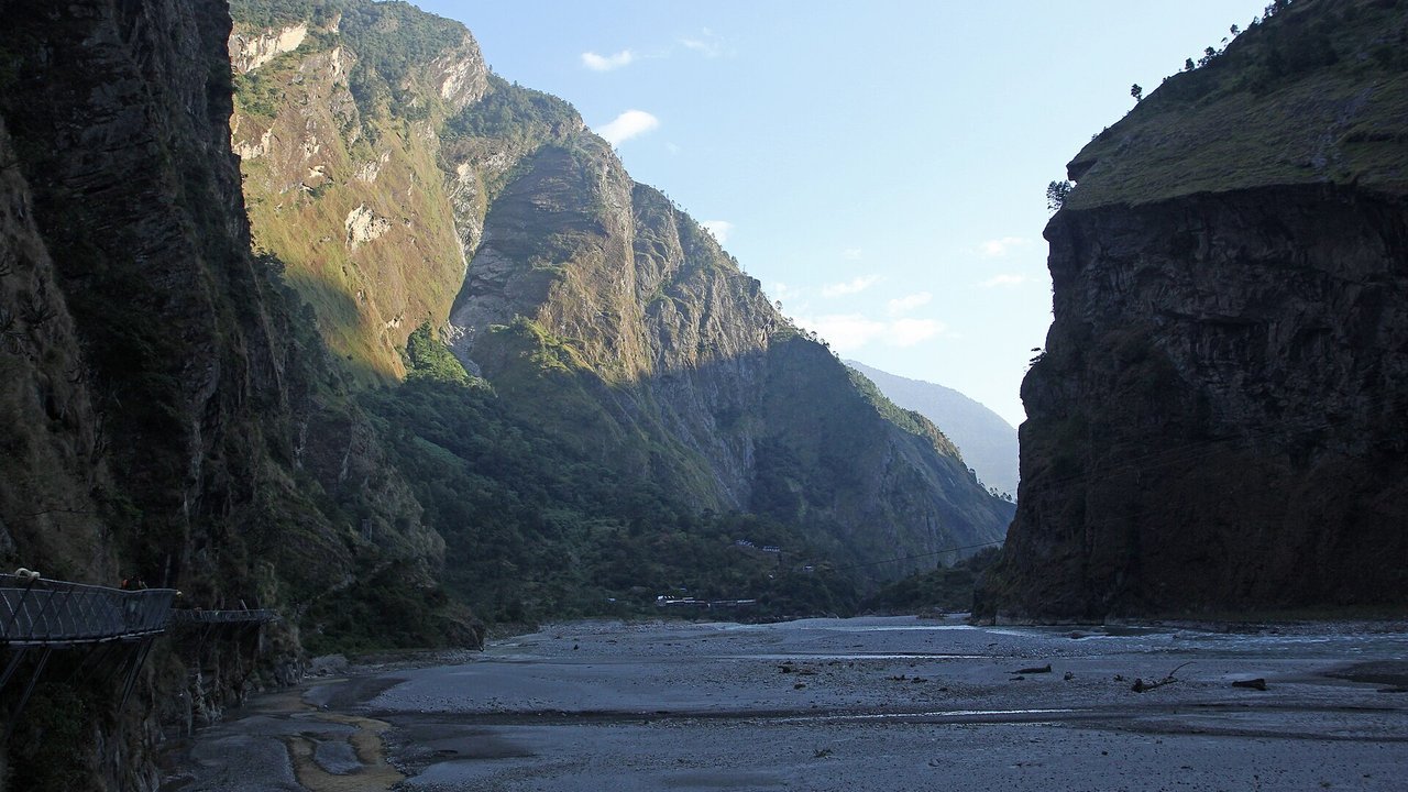 Stand-in, not a photo of this event: an October 2018 file photo of the Budhi Gandaki valley between Yaru Bagar and Jagat in Gorkha district, with a wide gravel riverbed between steep forested cliffs and a cliffside walkway on the left