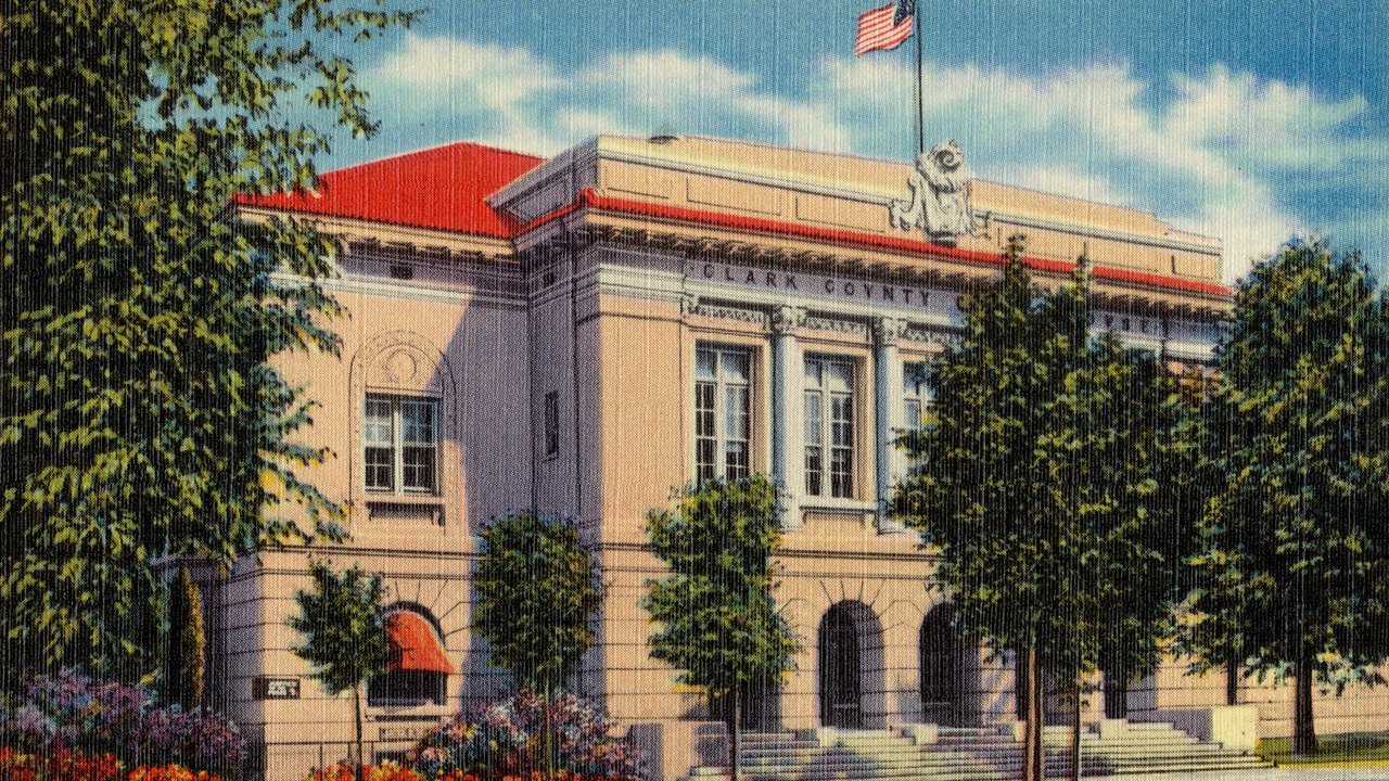 Stand-in, not a photo of this event: a circa 1930–1945 colour postcard of the old Clark County Court House in Las Vegas, a cream-coloured building with a red roof, arched entrances and a U.S. flag, framed by green trees
