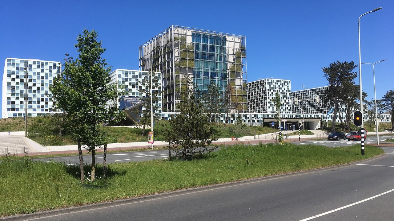 Stand-in, not a photo of this event: a May 2019 file photo of the International Criminal Court buildings in The Hague under a clear blue sky, with grass, trees and a road in front