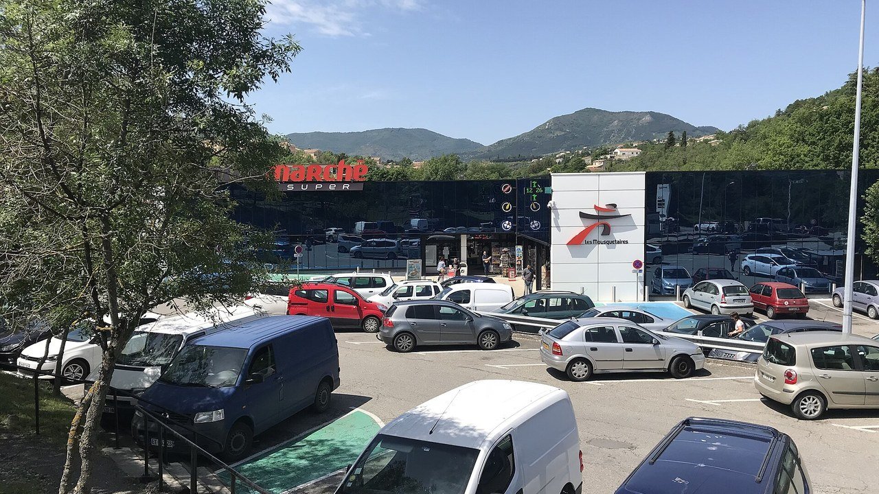 Stand-in, not a photo of this event: a May 2018 file photo of an Intermarché Super supermarket exterior in Privas, Ardèche, France, with a parking lot of cars, glass facade, Les Mousquetaires logo, green hills and blue sky