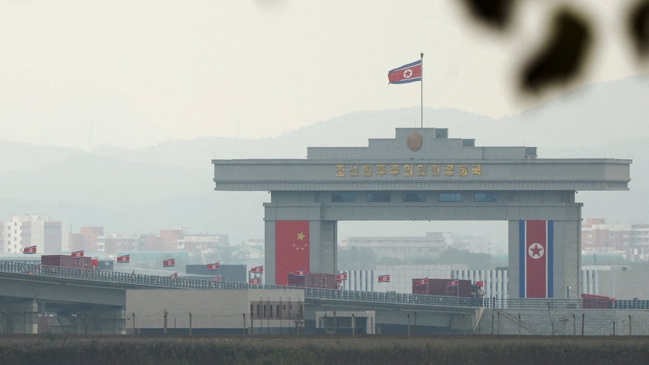 Freight trucks approach the border gateway arch displaying Chinese and North Korean flags on the New Yalu River Bridge linking Dandong, China, and Sinuiju, North Korea