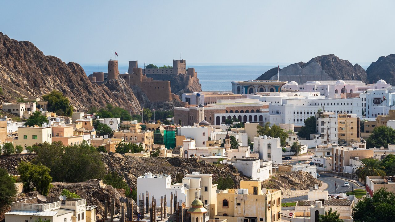 Stand-in: whitewashed buildings of old Muscat, Oman, below rocky hills and a hilltop fort, with the sea beyond, November 2024