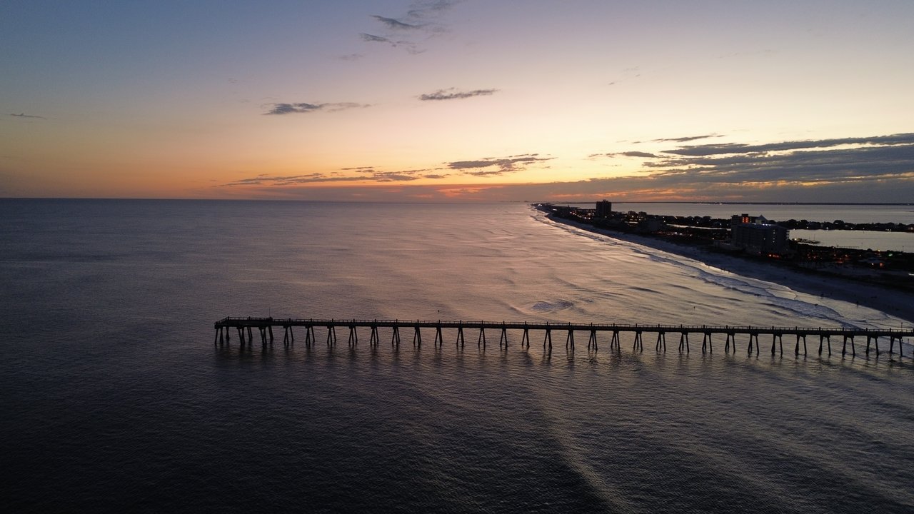 Stand-in, not a photo of this event: a March 2024 aerial file photo of the Gulf Pier at Pensacola Beach, Florida, at dusk, with calm water and a lit shoreline of buildings