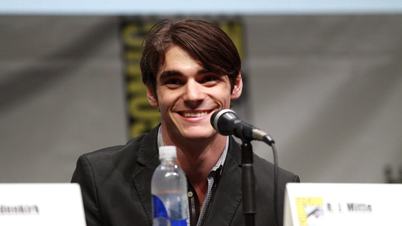 Stand-in, not a photo of this event: a July 2013 file photo of RJ Mitte smiling at a microphone during a Breaking Bad panel at San Diego Comic-Con, with a water bottle and a name card on the table
