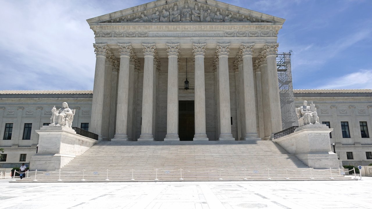 Stand-in, not a photo of this event: the white marble front of the U.S. Supreme Court Building in Washington on a sunny day in June 2024, with its columned portico, wide steps, two seated statues and a roped-off plaza, and scaffolding along the right side