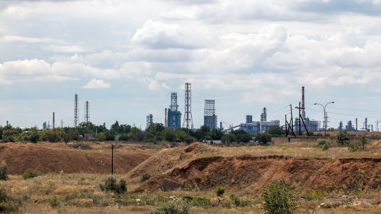 Archival stand-in: distant towers and chimneys of the Volgograd oil refinery behind dry, rolling ground under a cloudy sky, July 2023