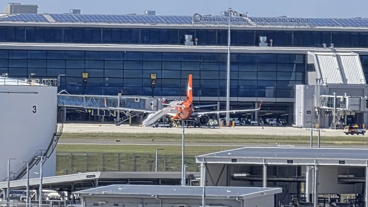 A Jetstar Airbus A320 sits on the apron in front of the glass terminal building bearing the Western Sydney International Airport sign at Badgerys Creek on Oct. 25, 2026